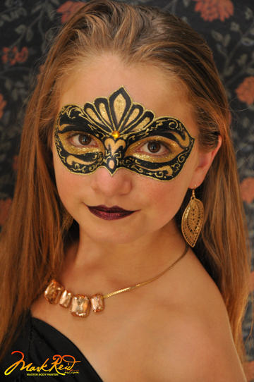 girl with a mask painted on around her eyes in black and gold that is very detailed